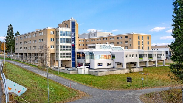 Un bâtiment moderne à plusieurs étages, doté de grandes fenêtres et arborant un grand panneau « SIX » sur sa façade.