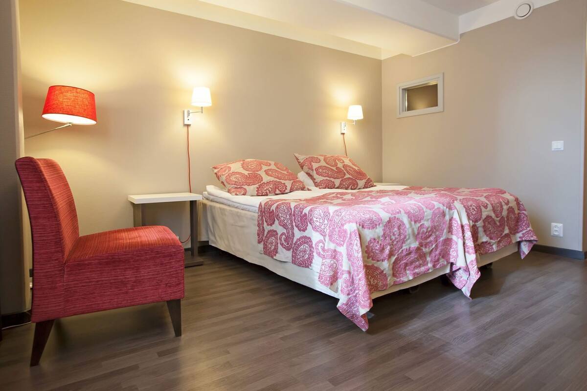 A bedroom with a bed, a chair, two wall-mounted lamps, and a small window.