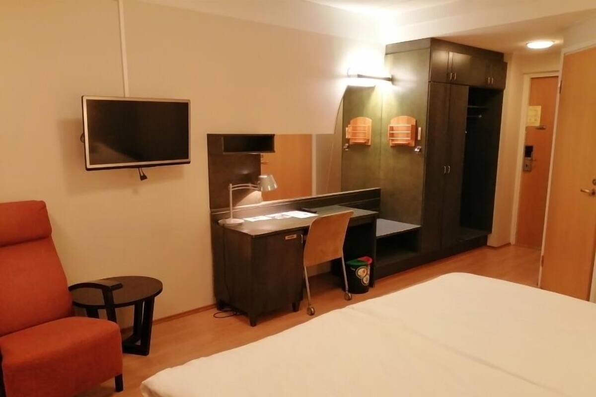 A hotel room with a bed, a desk, a chair, a TV, and a wardrobe.