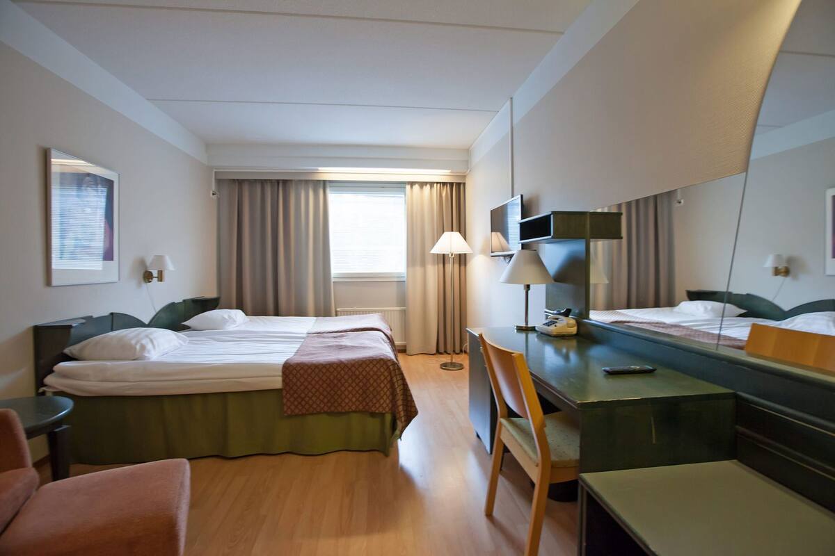 A hotel room with two beds, a desk, a chair, a lamp, and a mirror.