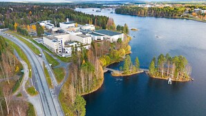 Vue aérienne d’un complexe immobilier moderne situé au bord d’un lac, avec plusieurs aires de stationnement et un pont reliant le complexe à une île.