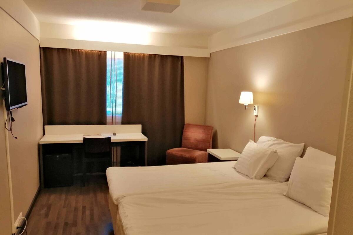 A hotel room with a bed, a desk, a chair, and a TV.