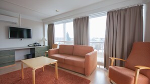 Une chambre d’hôtel moderne, équipée d’un canapé, d’un fauteuil et d’un téléviseur posé sur un meuble.