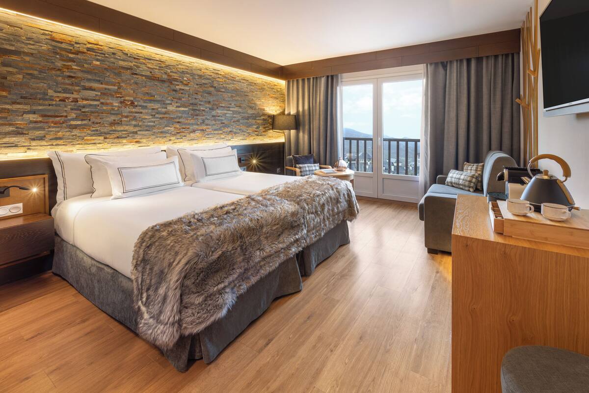 A modern hotel room with a large bed, a desk, a chair, and a balcony with a view.