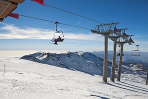 A ski lift with chairs suspended from cables, a snowy mountain slope, and a clear sky.
