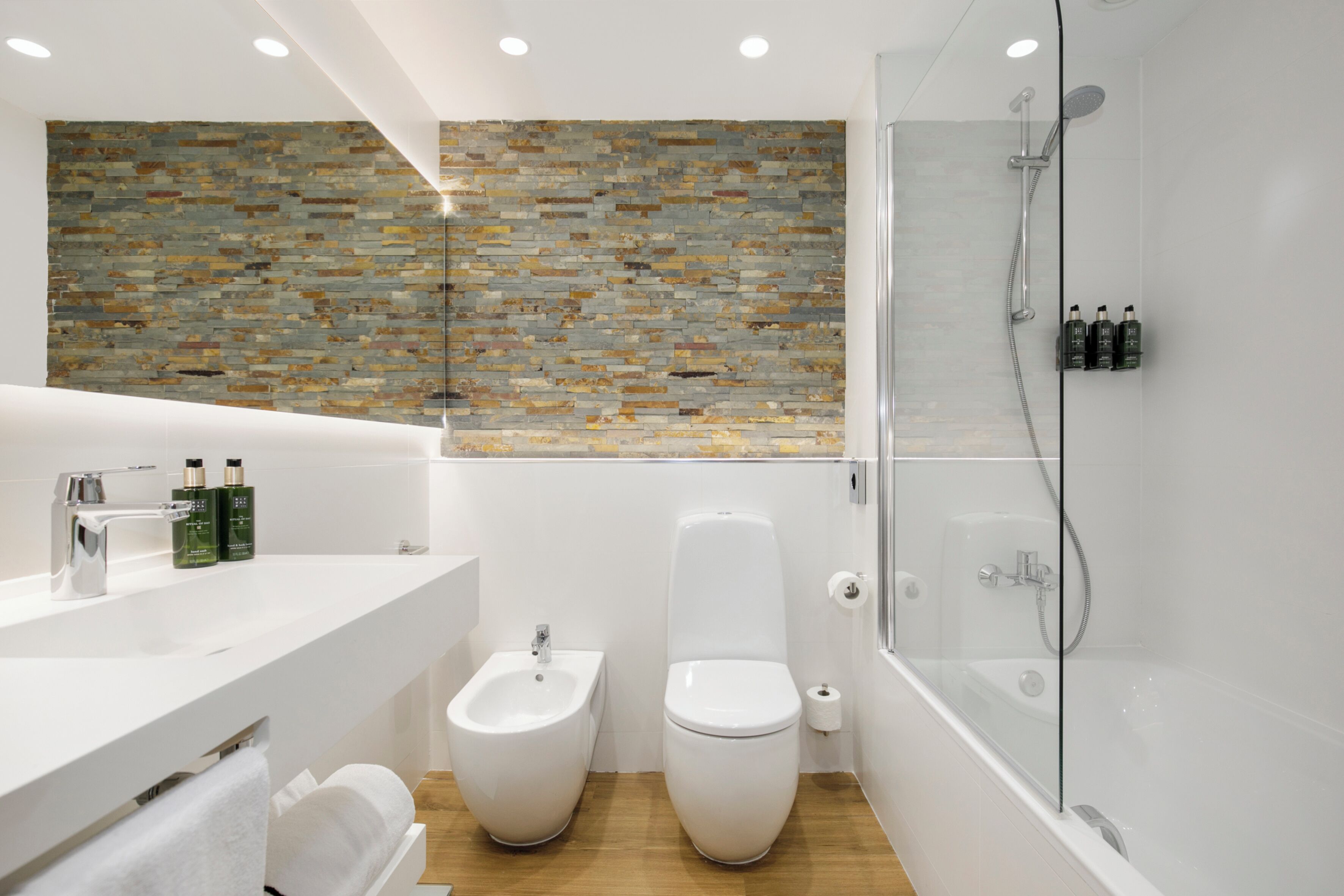 A modern bathroom with a stone mosaic backsplash, a glass-enclosed shower, and a white vanity with toiletries.