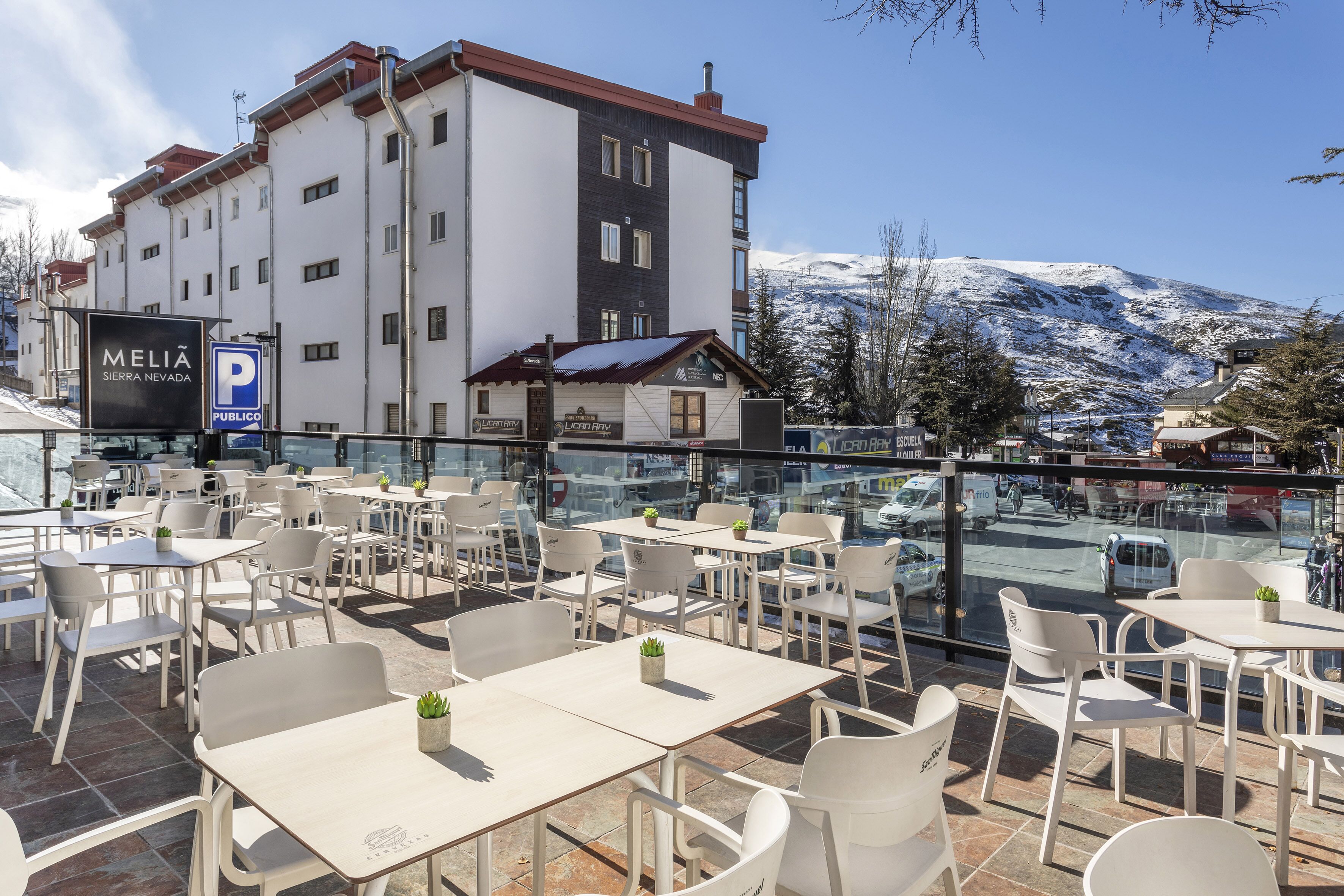 A terrace with outdoor seating, a view of a snow-capped mountain, and a building with signage for 'MELIA SIERRA NEVADA'.