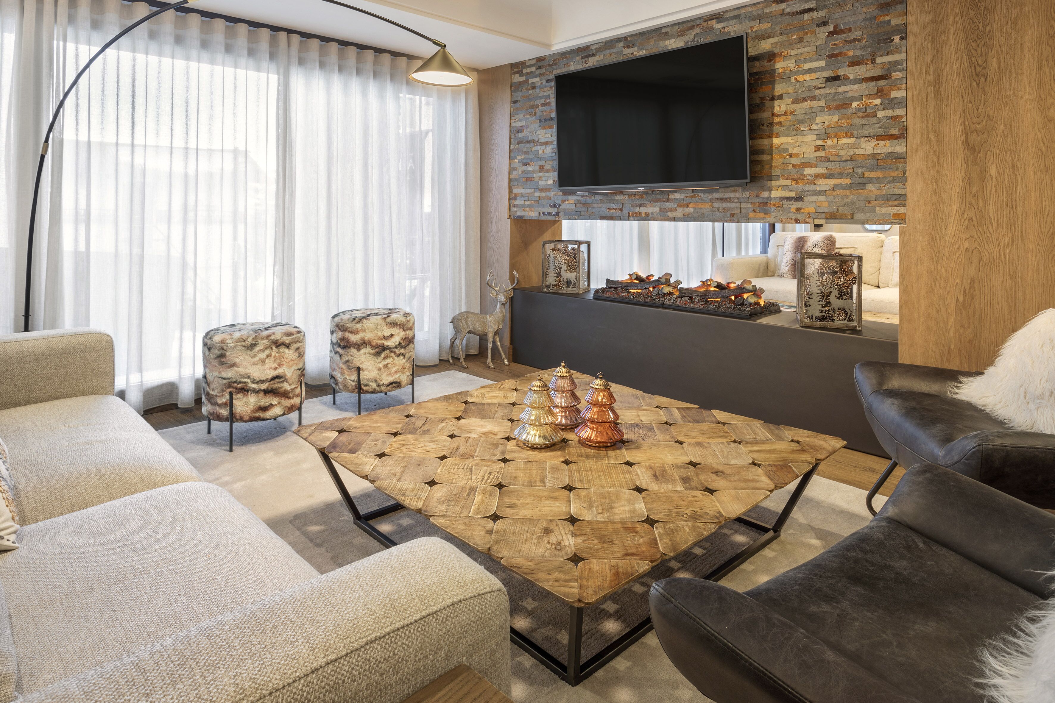 A modern living room with a large wooden coffee table, leather sofas, and a mounted TV.