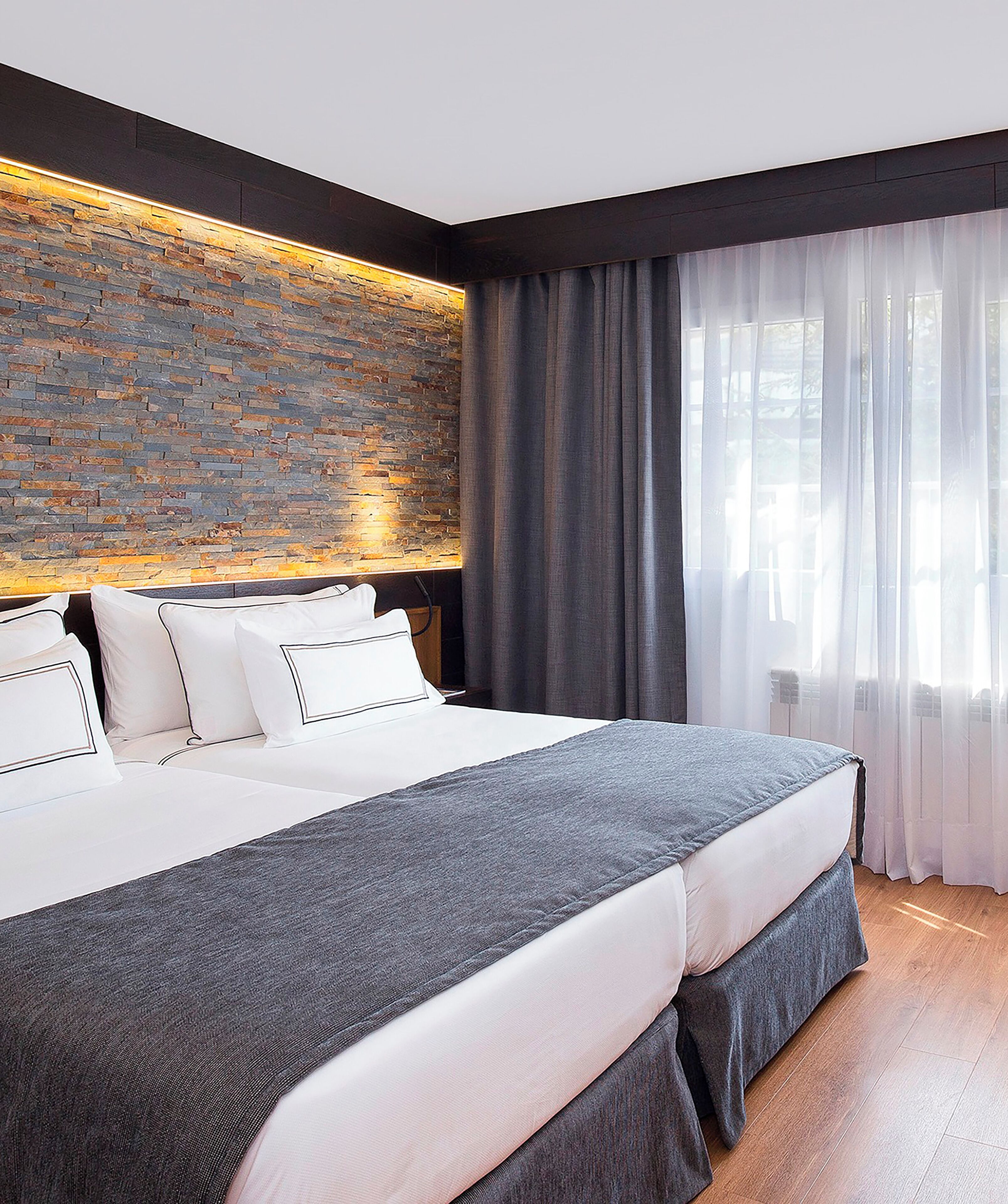 Una habitación de hotel moderna con una cama grande, un muro decorativo de piedra y cortinas de gasa.