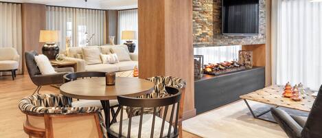 A modern living room with a round dining table, wooden chairs, a sofa, and a flat-screen TV mounted on a brick wall.