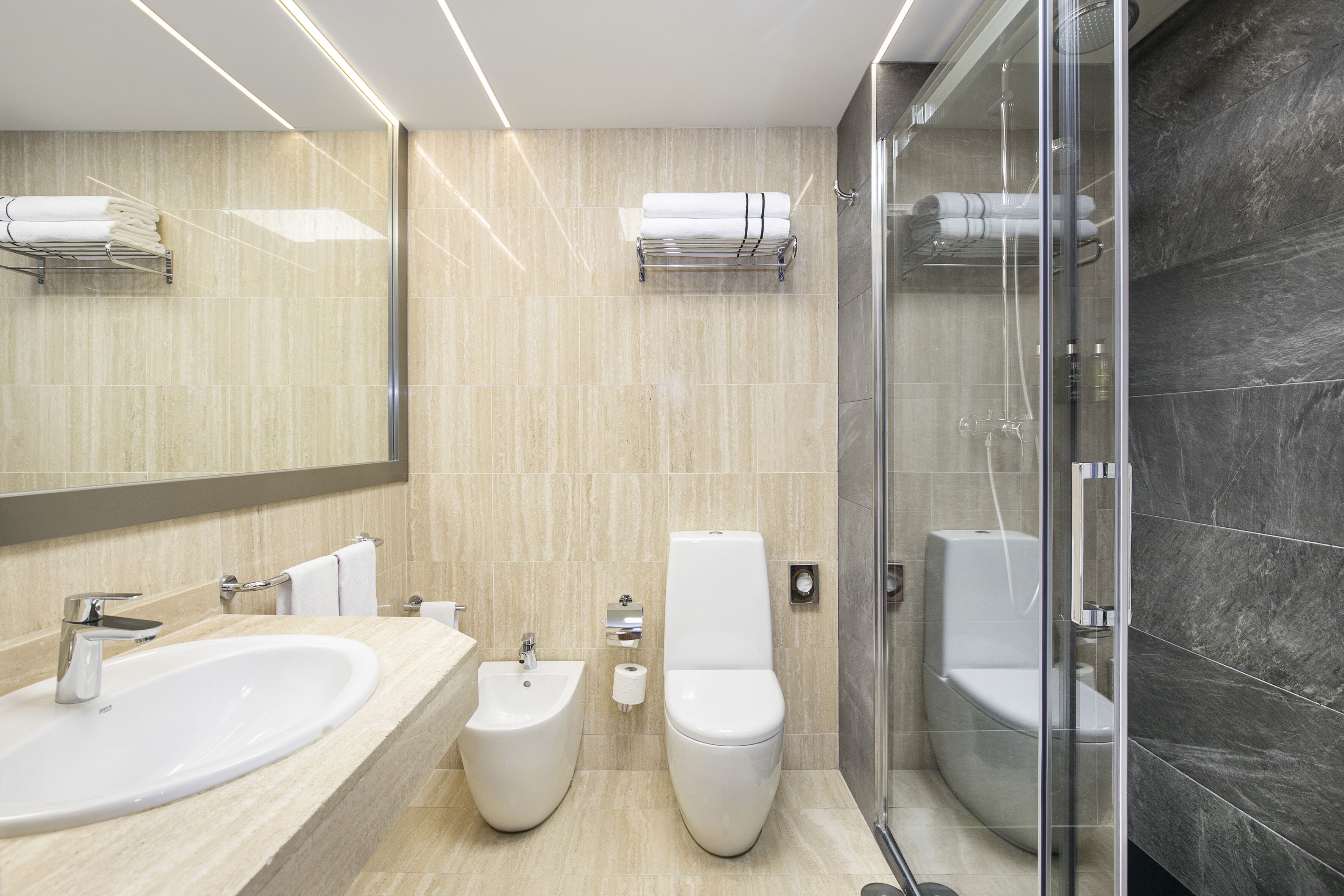 Un bany modern amb un envàs gran, bidet, vàter i dutxa amb panells de vidre.