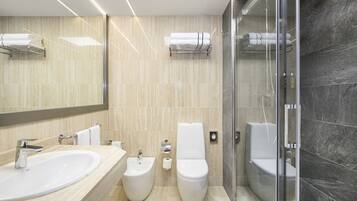 Un bany modern amb un envàs gran, bidet, vàter i dutxa amb panells de vidre.