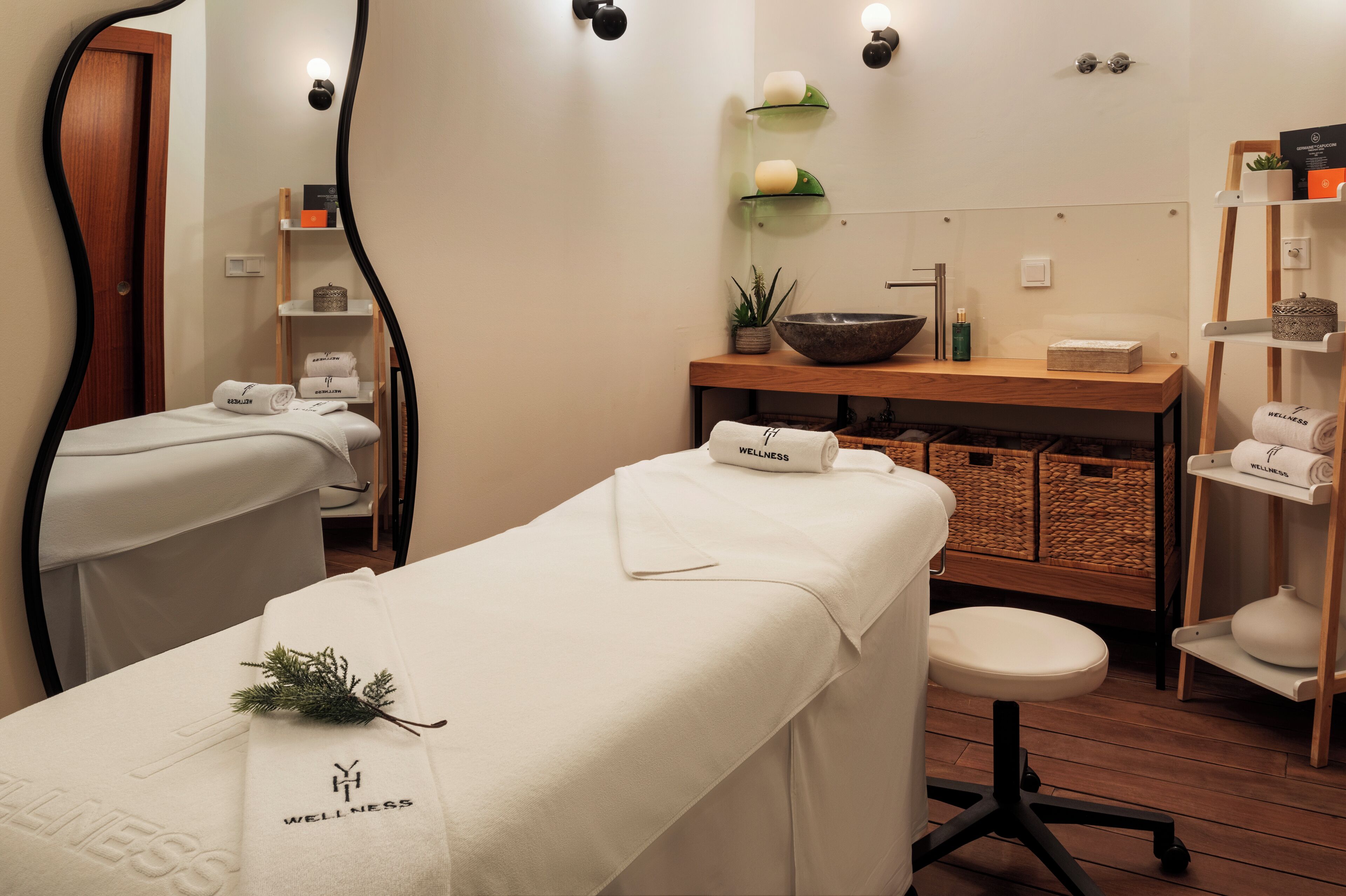 A wellness room with two massage tables, a wooden bench, a sink, and shelves with wellness products.