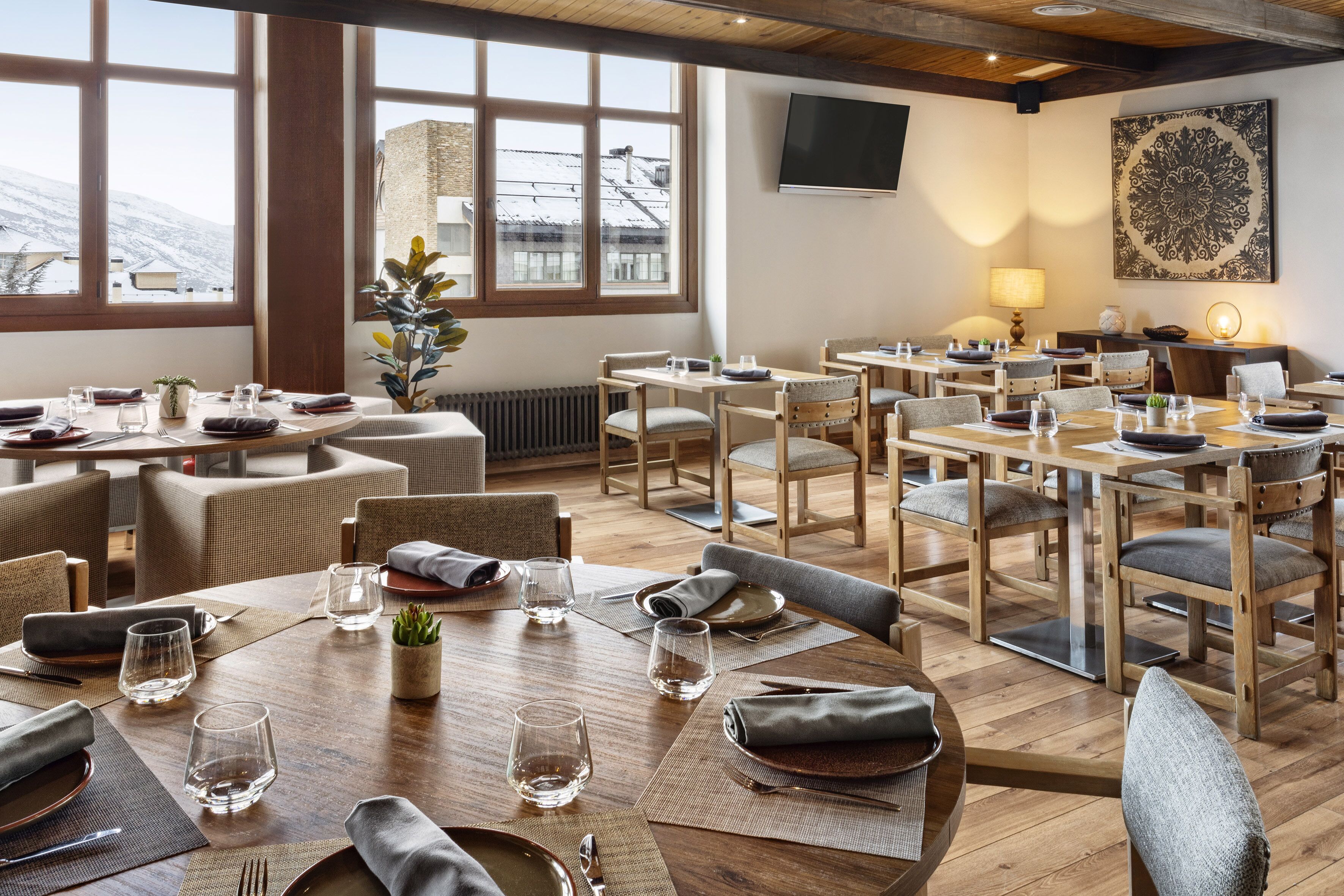 Un restaurant amb diverses taules i cadires, finestres grans que donen vista a edificis coberts de neu, i un televisor de pantalla plana penjat a la paret.