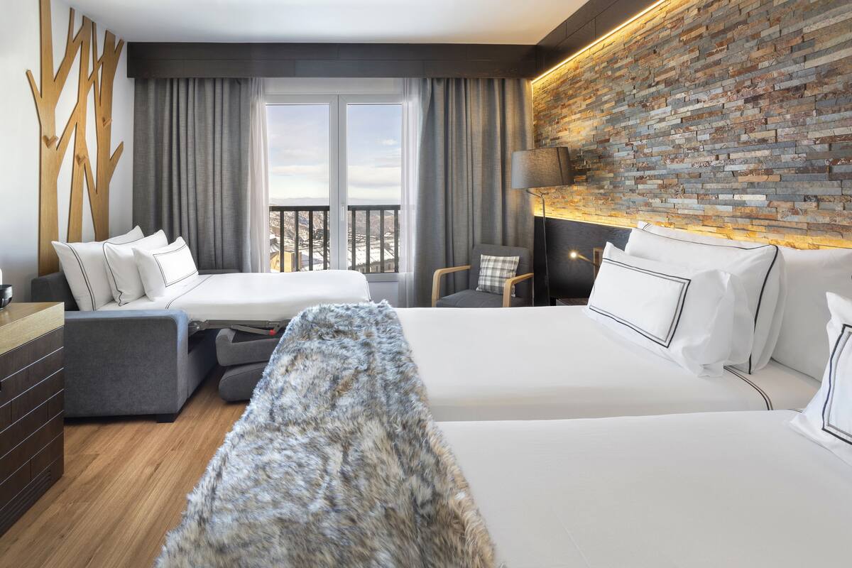 A hotel room with two beds, a sofa, a small table, and a view of the city.