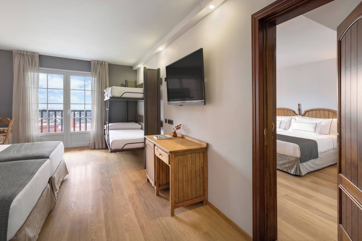 A hotel room with a bed, a desk, a TV, and a balcony with a view.