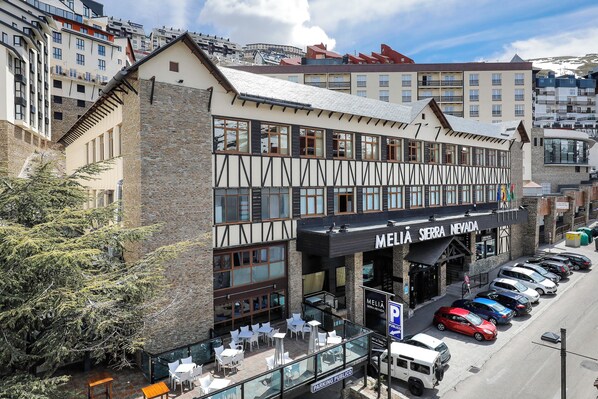 A hotel with a traditional facade, outdoor seating, and a parking area.