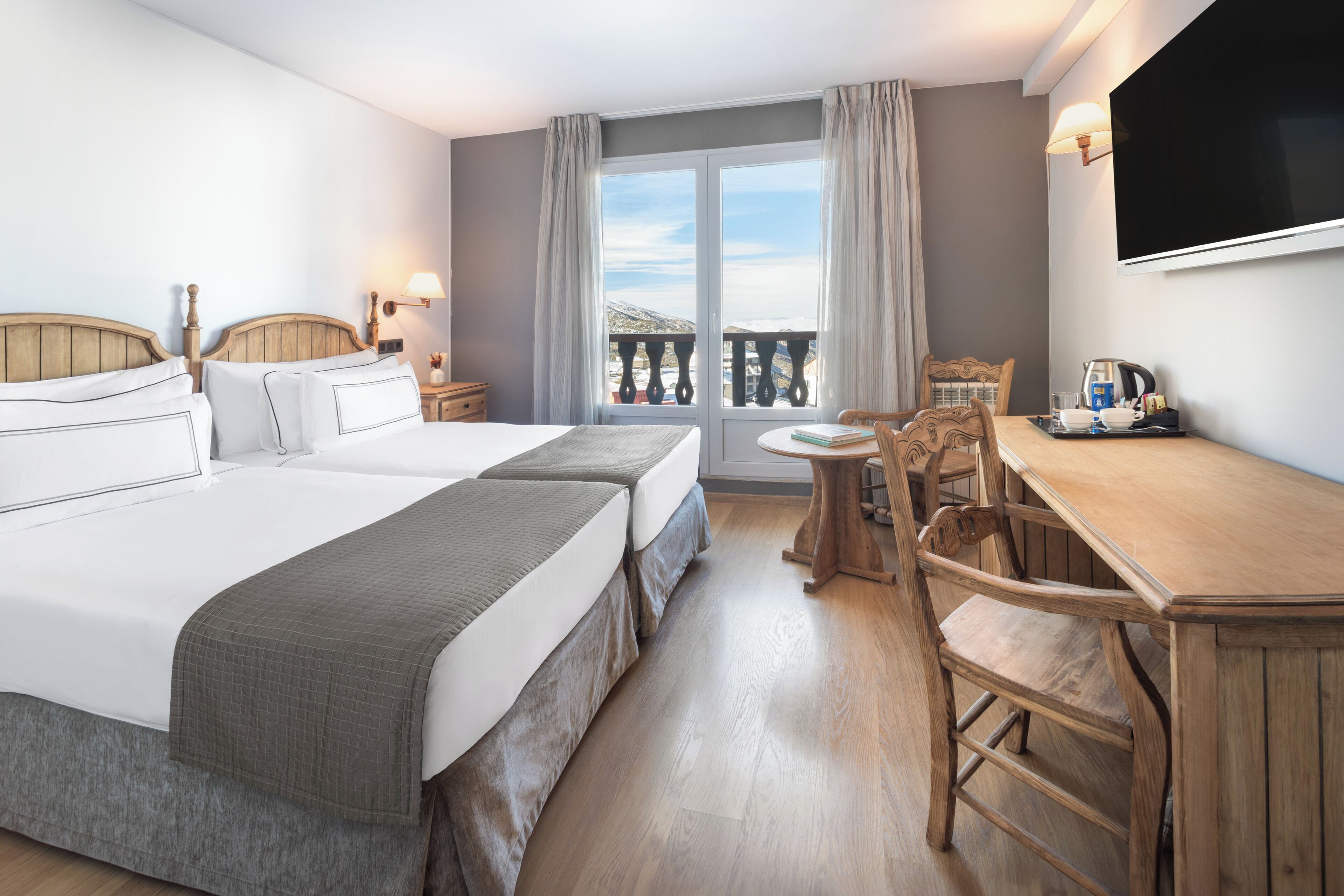 A hotel room with two beds, a balcony with a view, a wooden desk, and a TV.