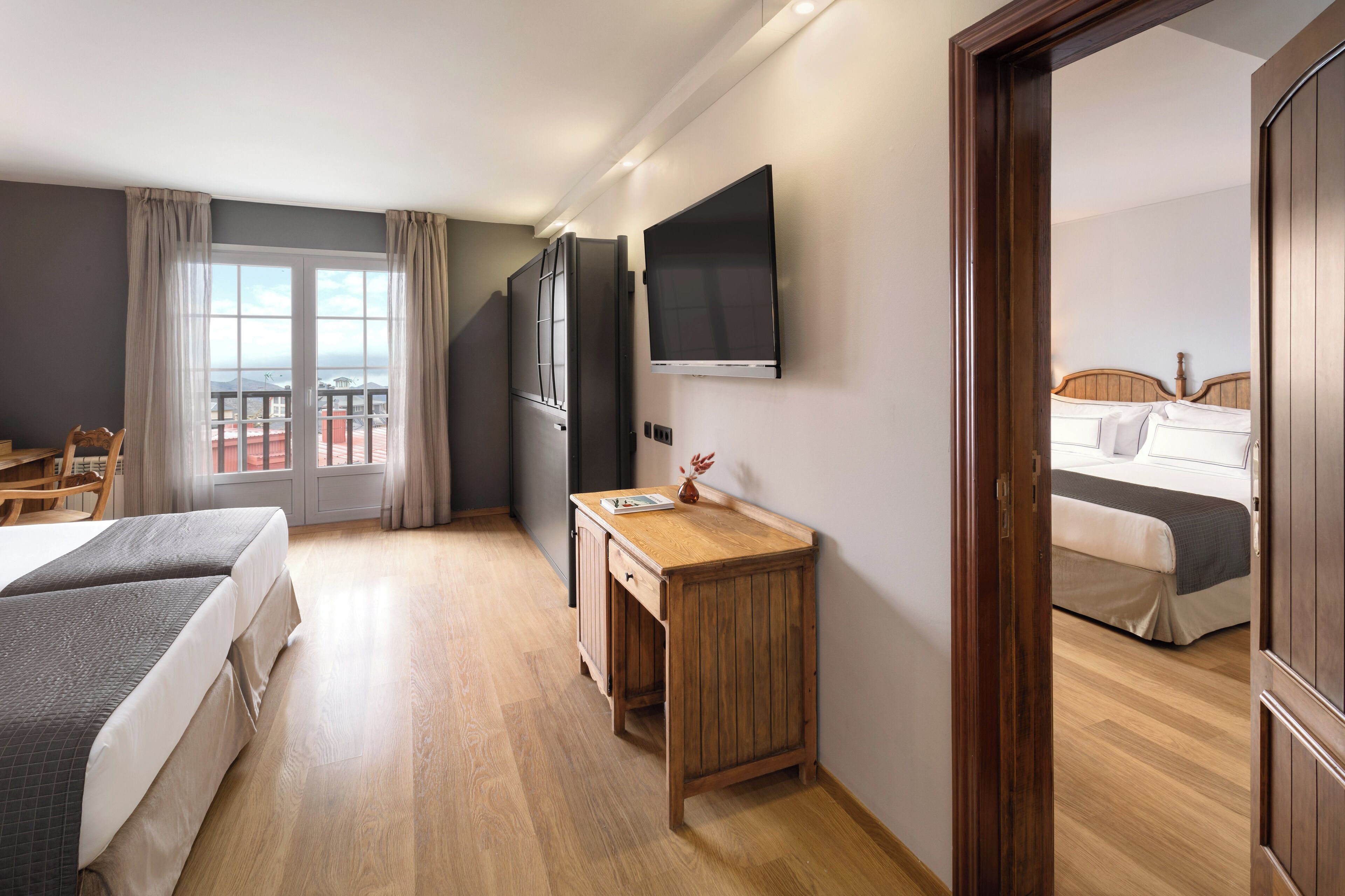 A hotel room with a bed, a desk, a TV, and a view of the city.