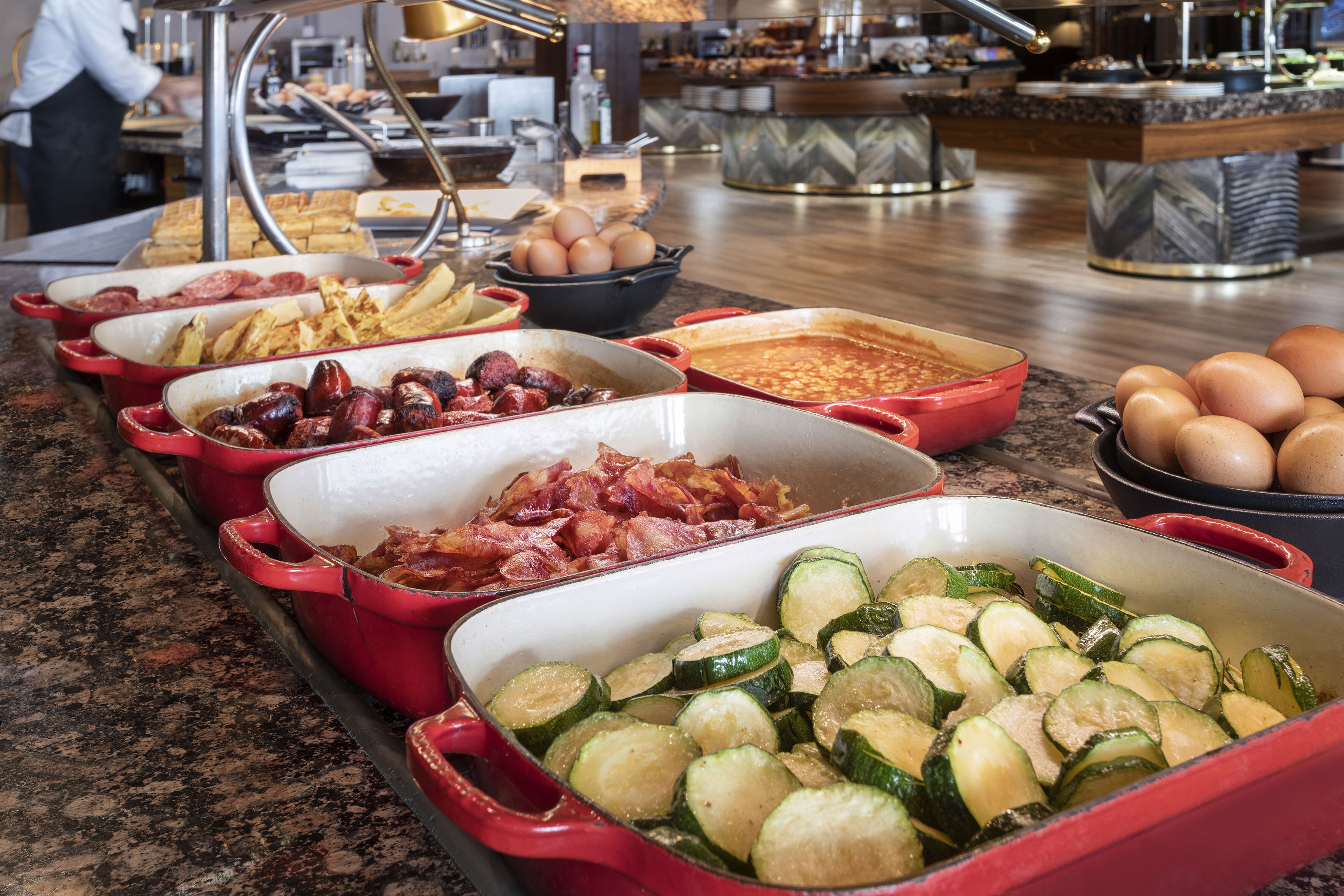 Buffet amb diferents plats, incloent bacon, ous i verdures a làmines.