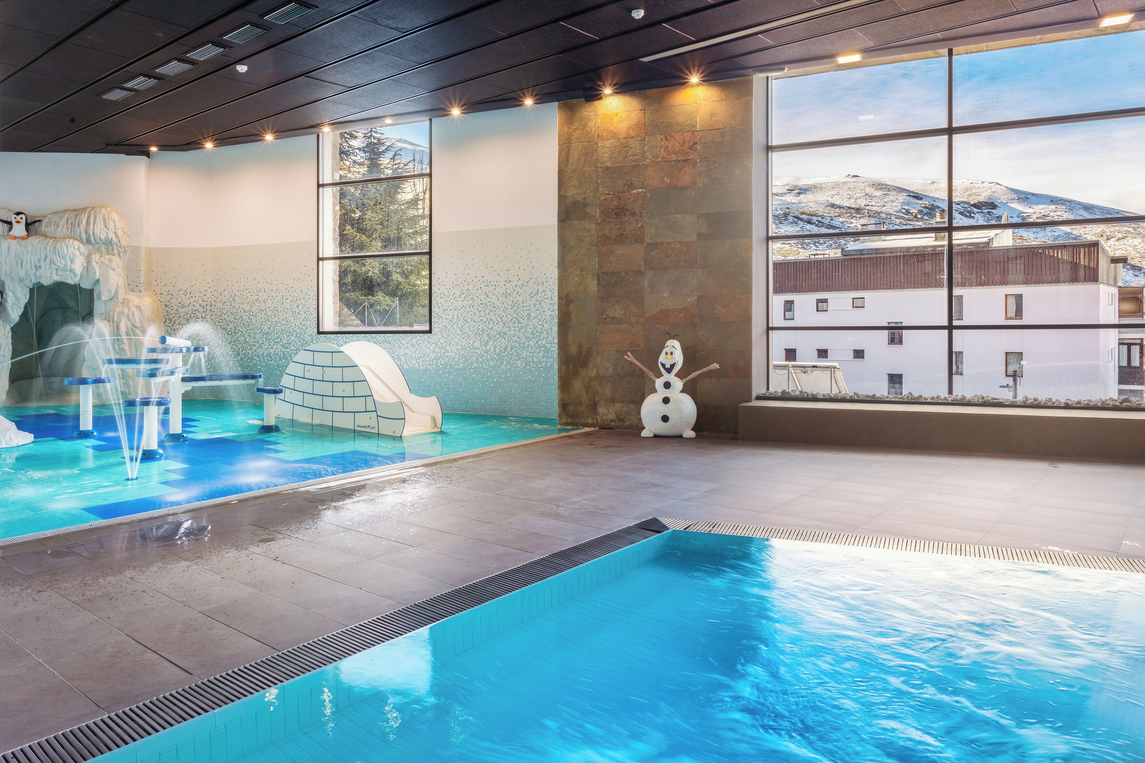 Una piscina interior con tobogán, una bañera de hidromasaje y vistas a una montaña nevada.