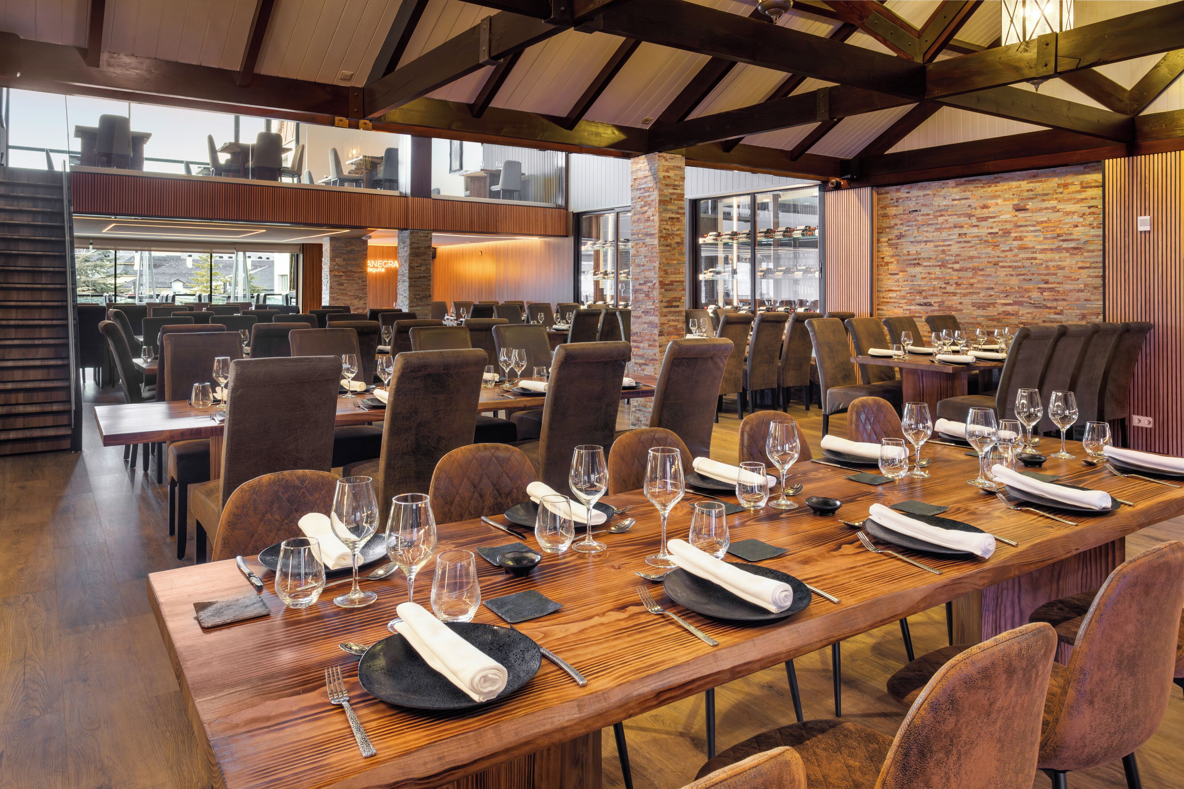 Un restaurante con mesas de madera largas dispuestas para comer, que presenta una pared de ladrillo y vigas de madera.