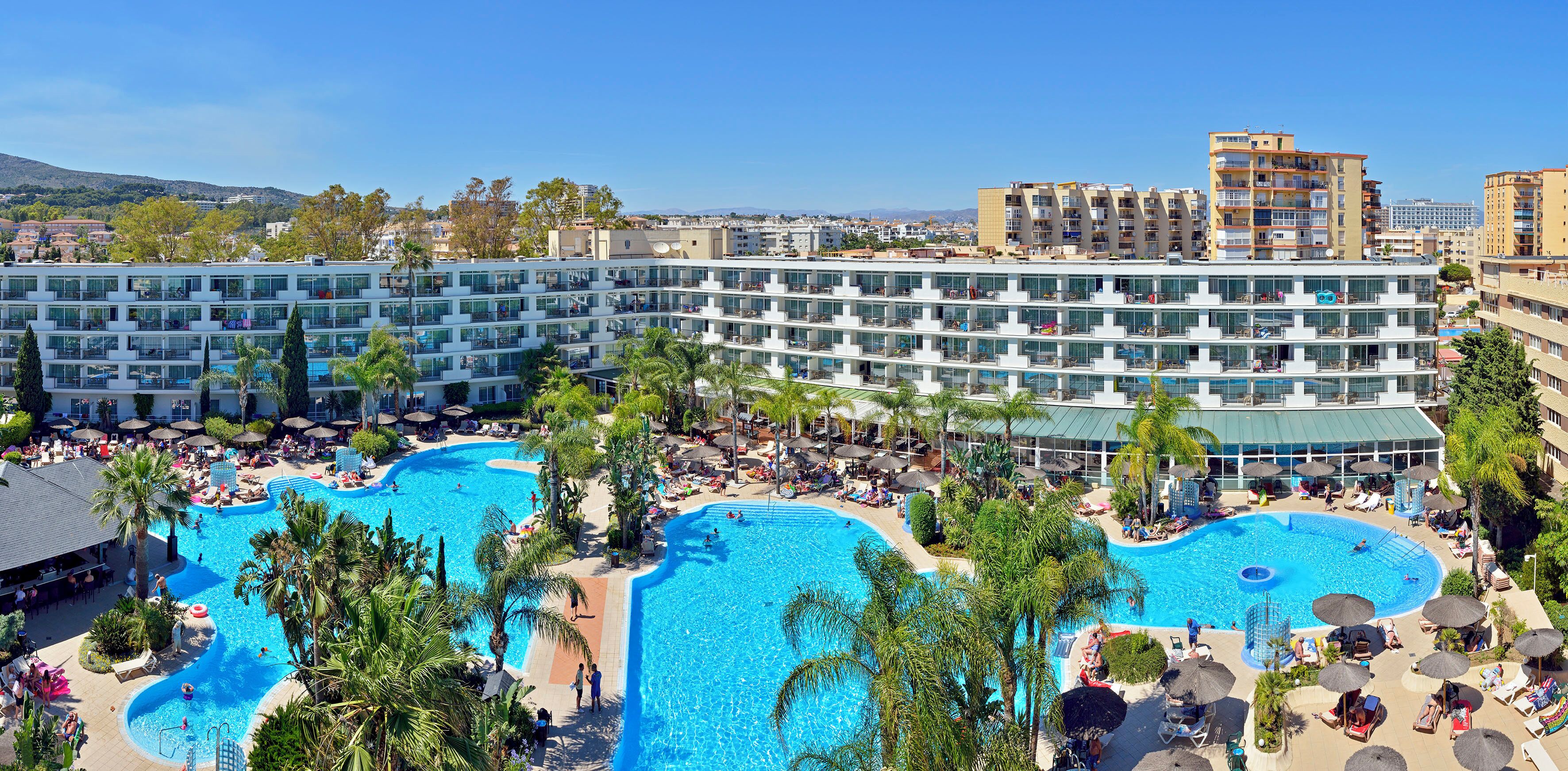 Un hotel con múltiples piscinas, un bar en la azotea y vistas a la ciudad.