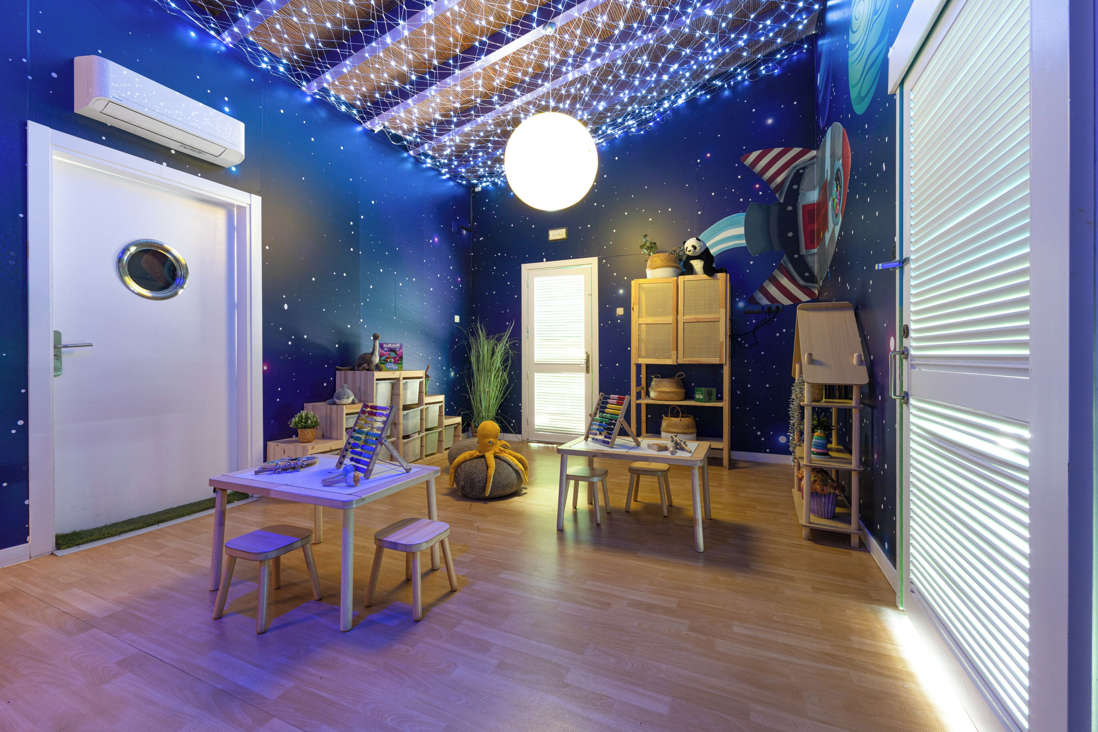 A room with a starry ceiling, wooden flooring, a round table with chairs, and a bookshelf.
