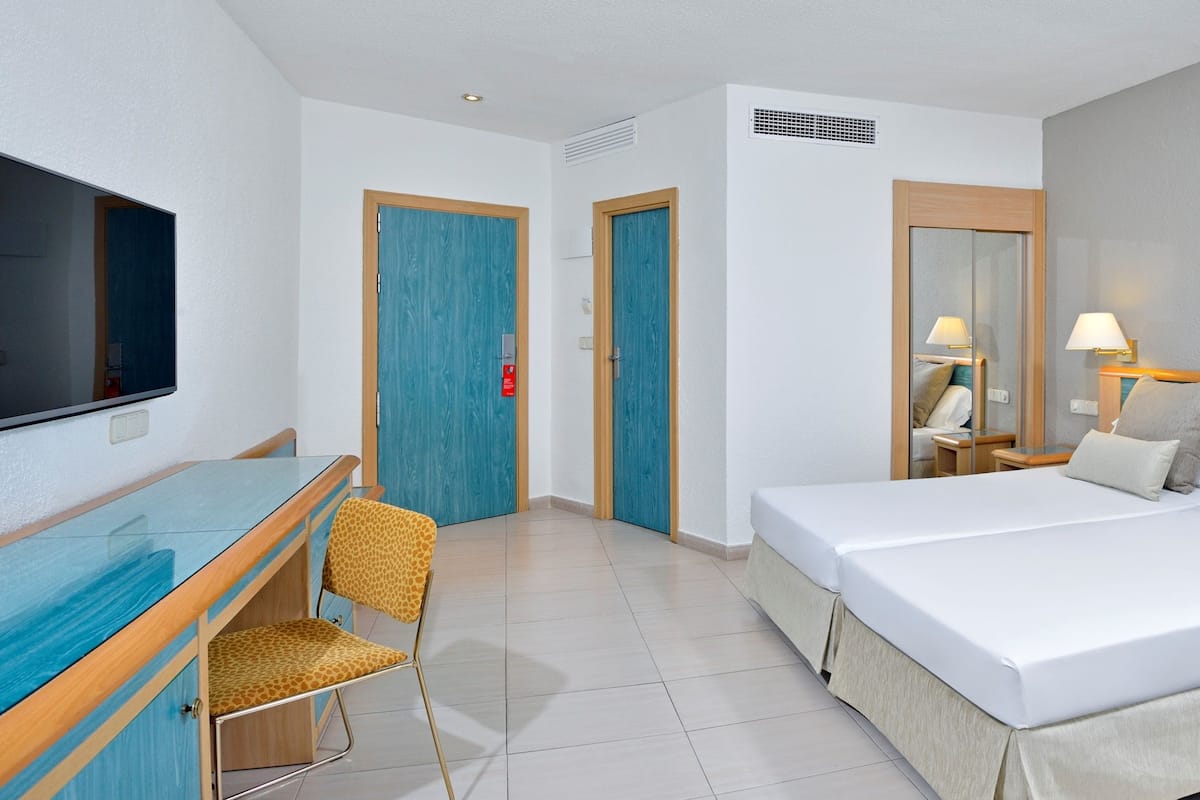 Habitación de hotel con cama, mesitas de noche, escritorio con silla, televisor y espejo.