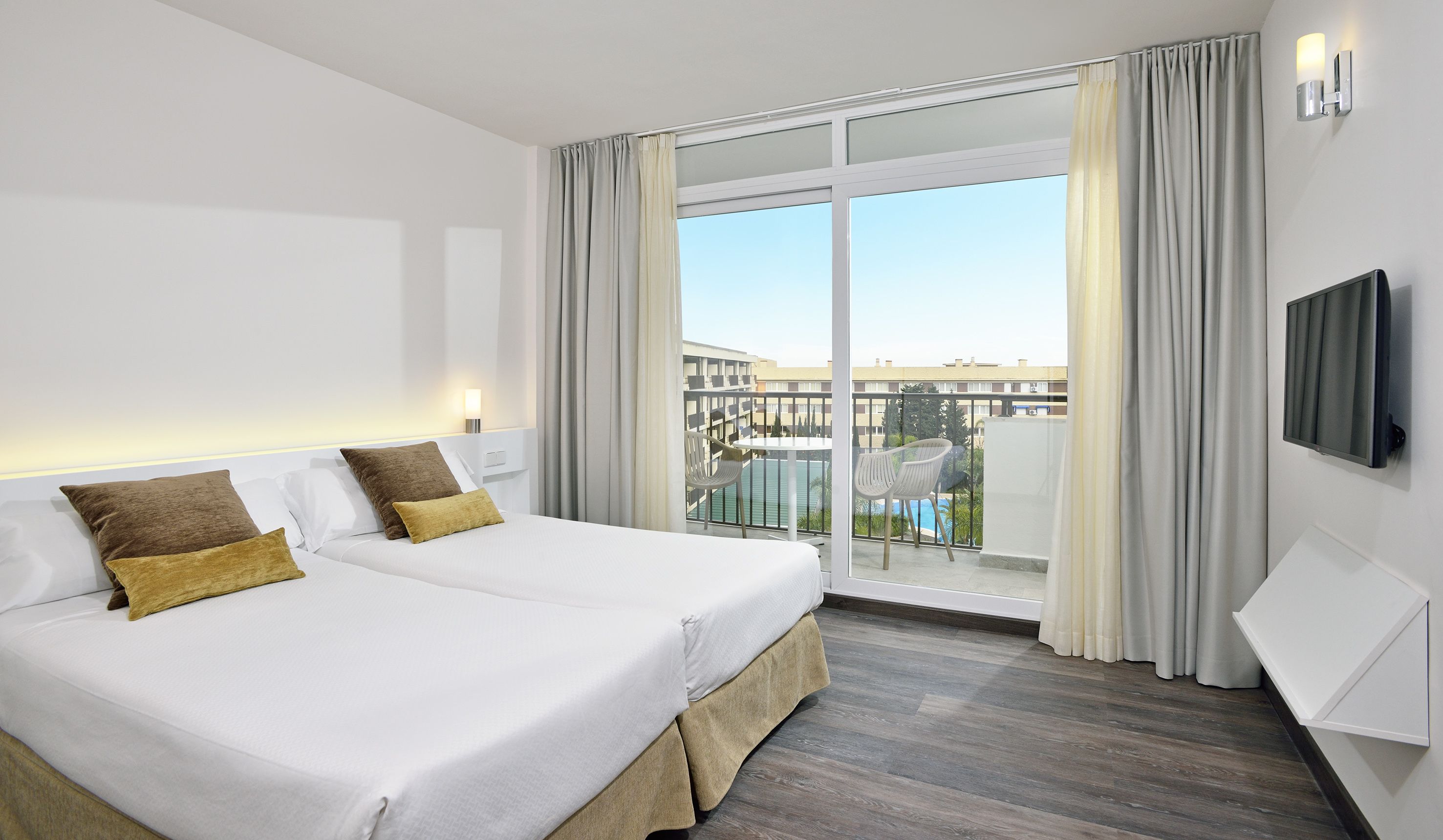 A hotel room with a large bed, a TV, and a balcony with a pool view.