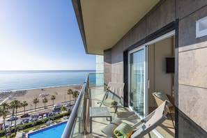 A balcony with a view of the beach and ocean, a pool, and lounge chairs. - Sol Principe (Torremolinos)