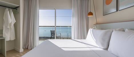 Habitación de hotel con una cama grande, una silla, una mesa y vista al mar.
