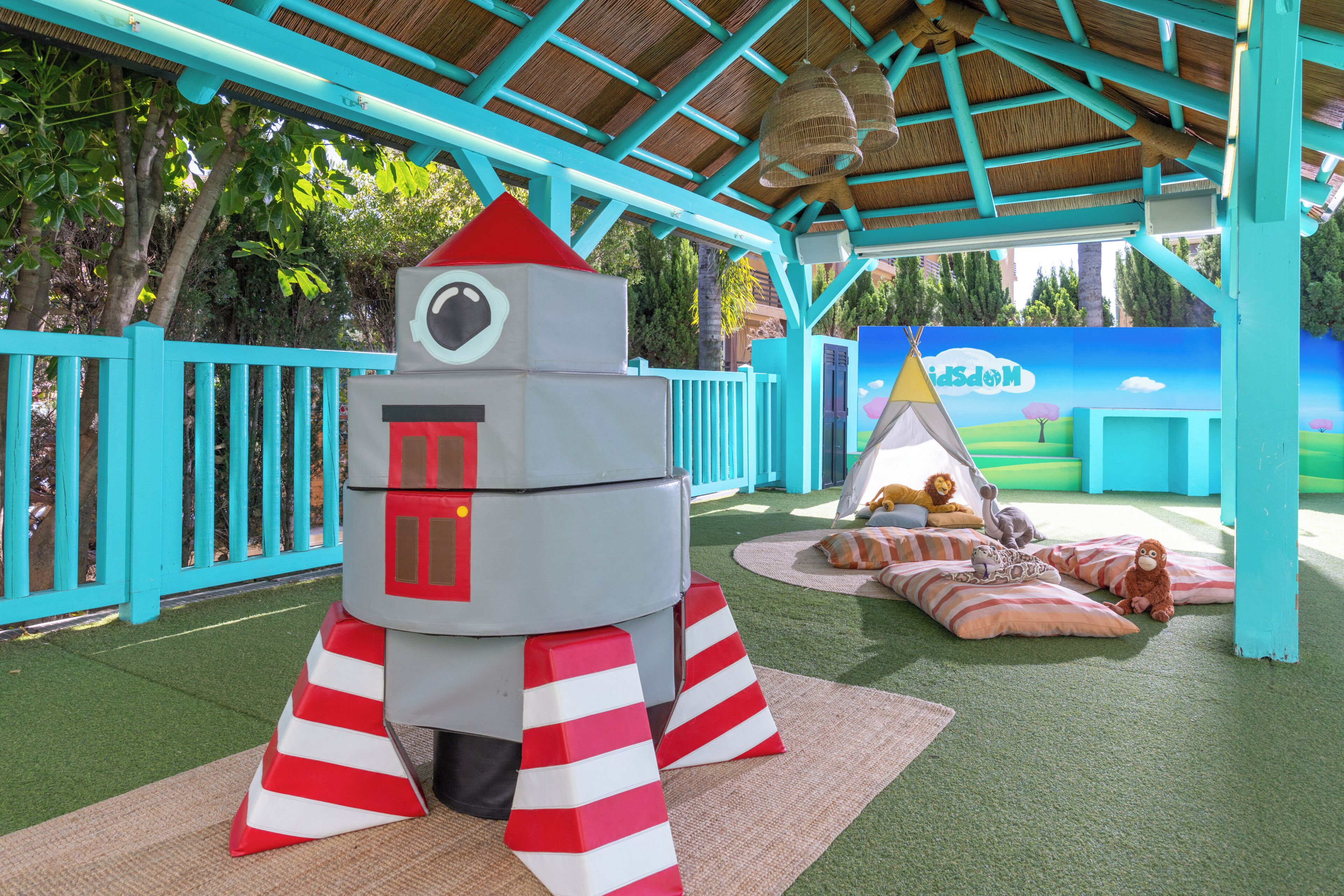 A play area with a rocket-shaped play structure, a tent, and a mural in the background.
