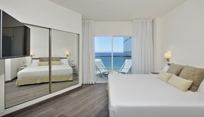 Relax in this spacious room with a large bed, a smaller bed, and a seating area, featuring a balcony with ocean views.