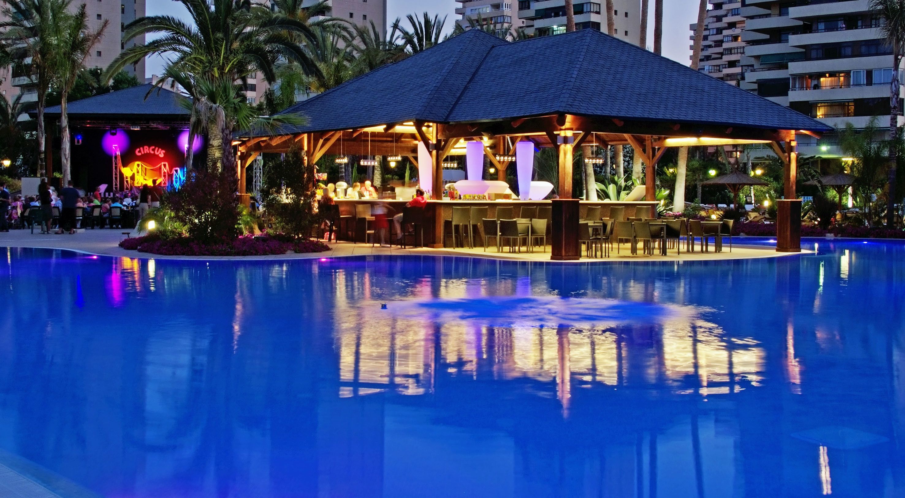 Un área junto a la piscina con un bar techado y sillones de descanso.