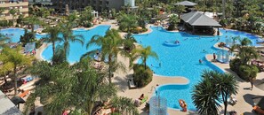 Una gran piscina al aire libre rodeada de palmeras y zonas de descanso.