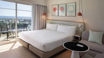 Habitación de hotel con una cama grande, un sofá, una mesita y un balcón con vistas a la ciudad.