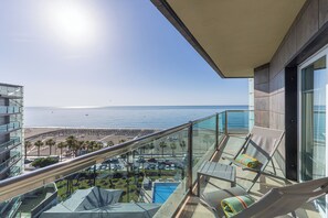 Un balcon doté d’une rambarde en verre, offrant une vue sur une piscine et une plage.