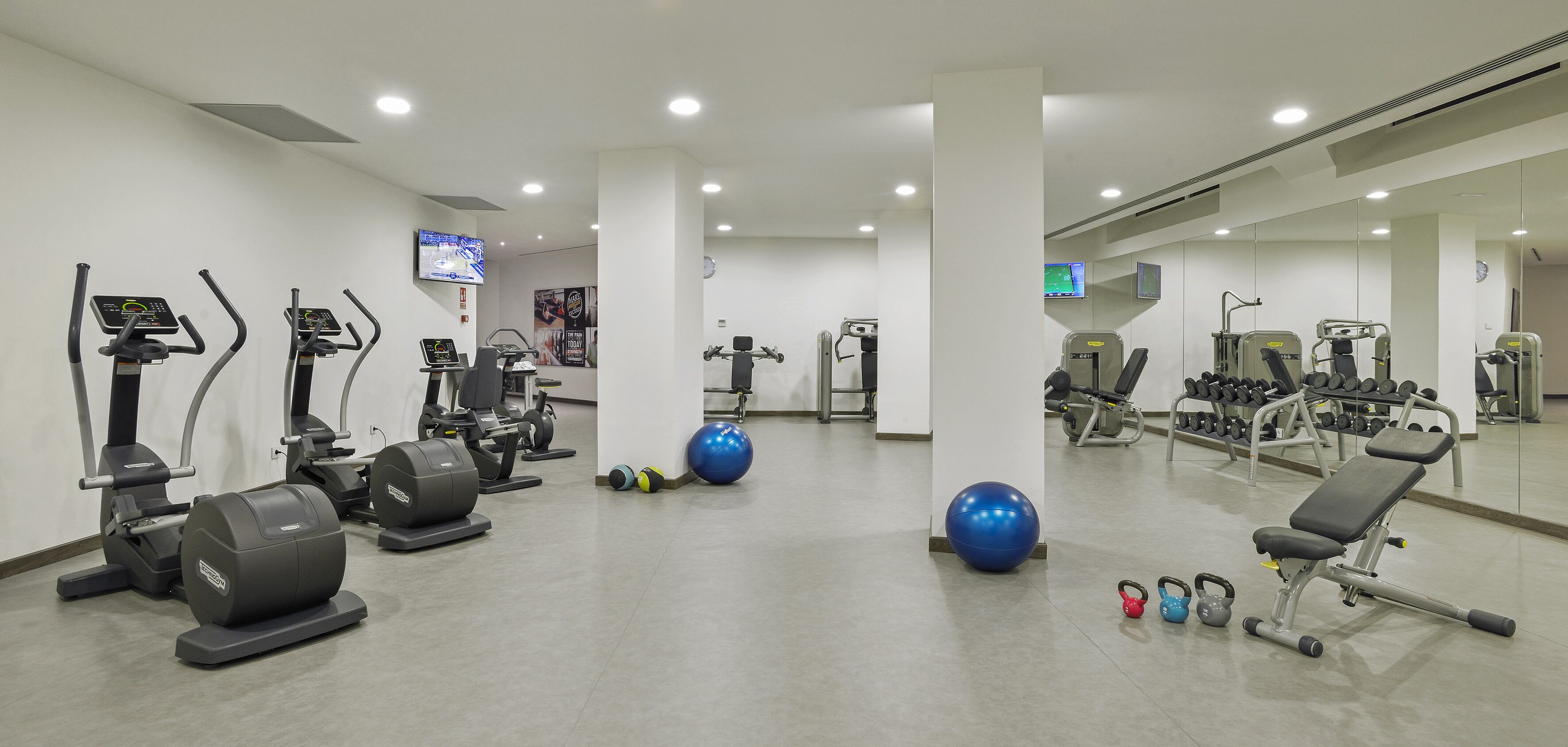 Un gimnasio con diverso equipamiento de ejercicio, incluyendo cintas de correr, pesas y pelotas de entrenamiento.