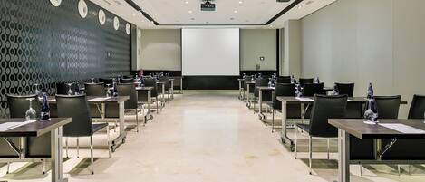 A conference room with a large screen, rows of tables with chairs, and a patterned wall.