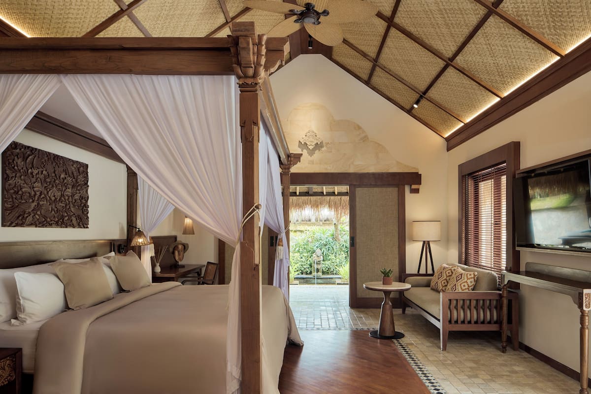 Ein Schlafzimmer mit Baldachinbett, Sofa, Fernseher und Blick ins Freie.