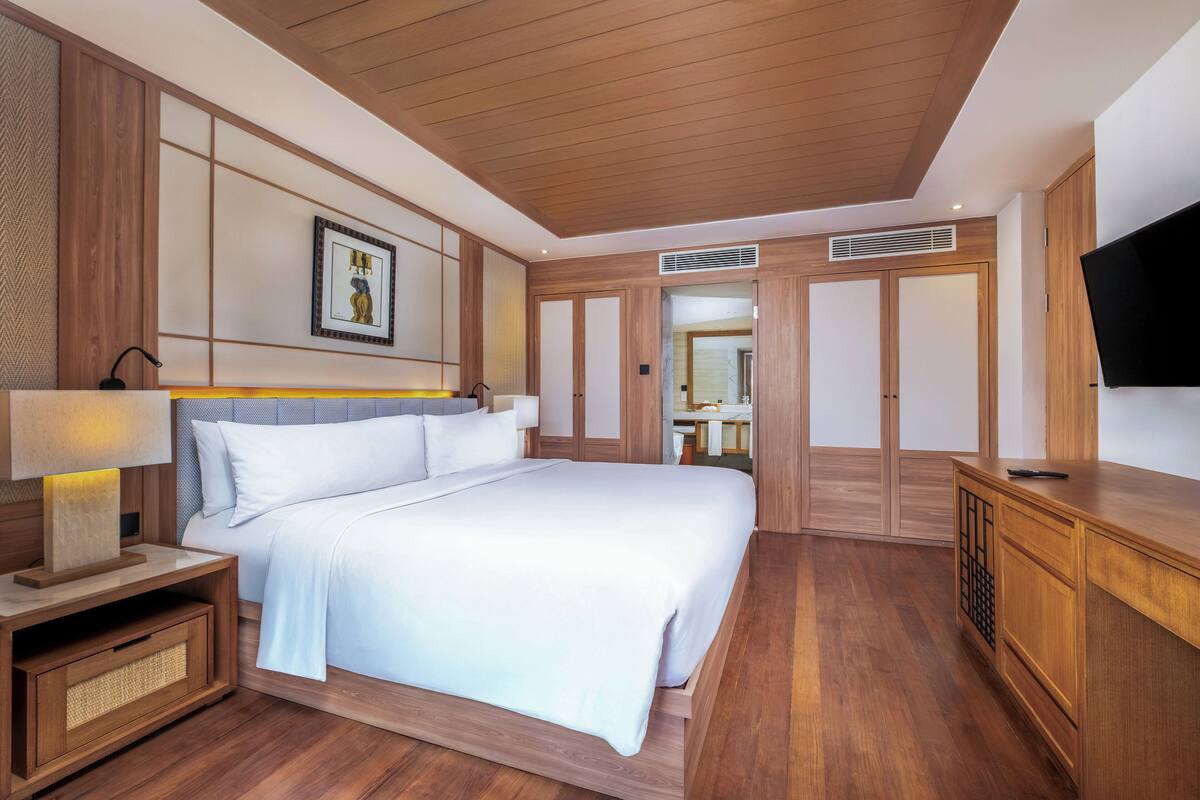 Ein modernes Hotelzimmer mit einem großen Bett, Holzböden, einem Flachbildfernseher und einer Wandverkleidung im traditionellen Stil.