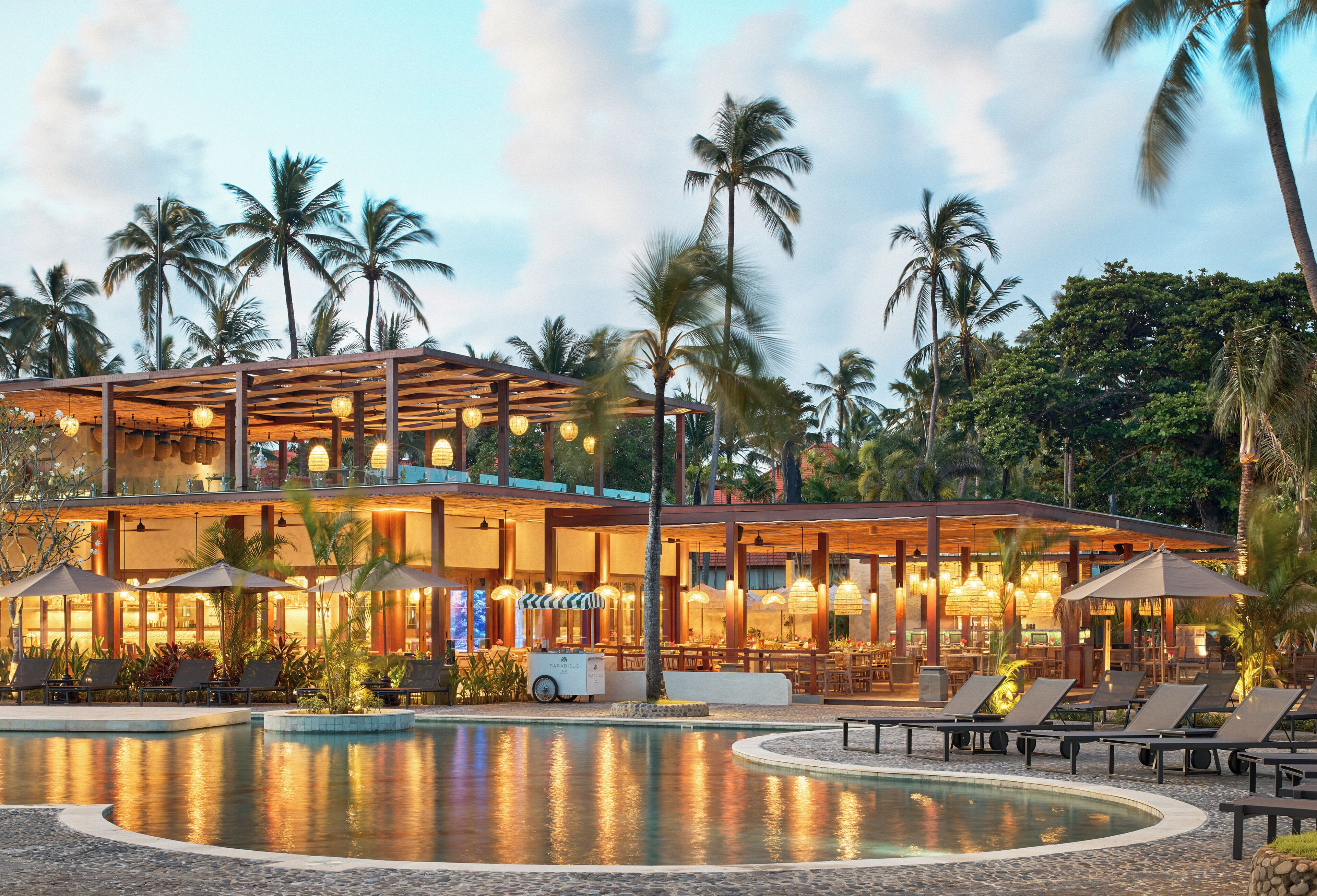 A resort with a pool, lounge chairs, and palm trees.