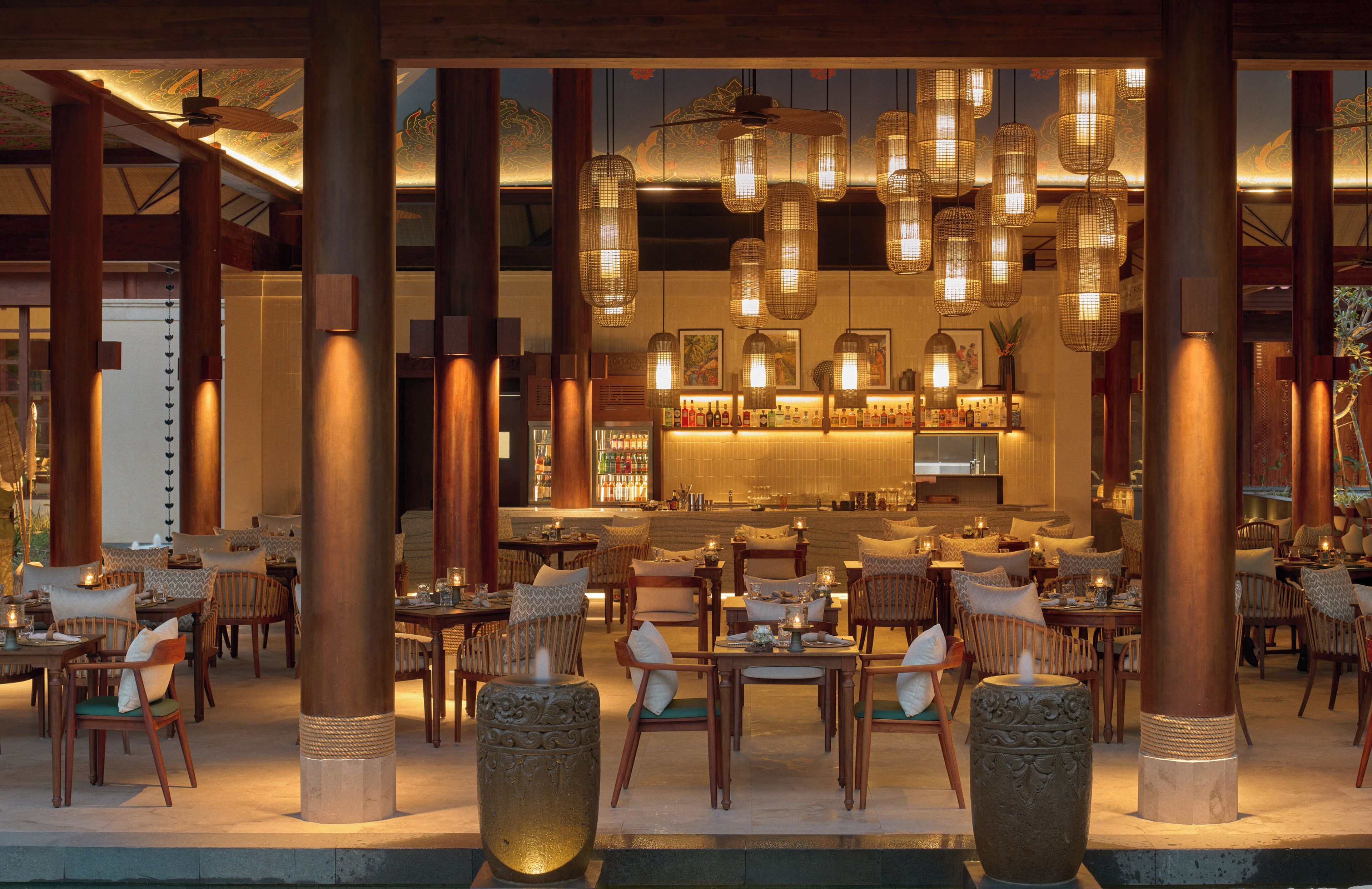 A restaurant with multiple tables and chairs, a bar area, and decorative hanging lights.
