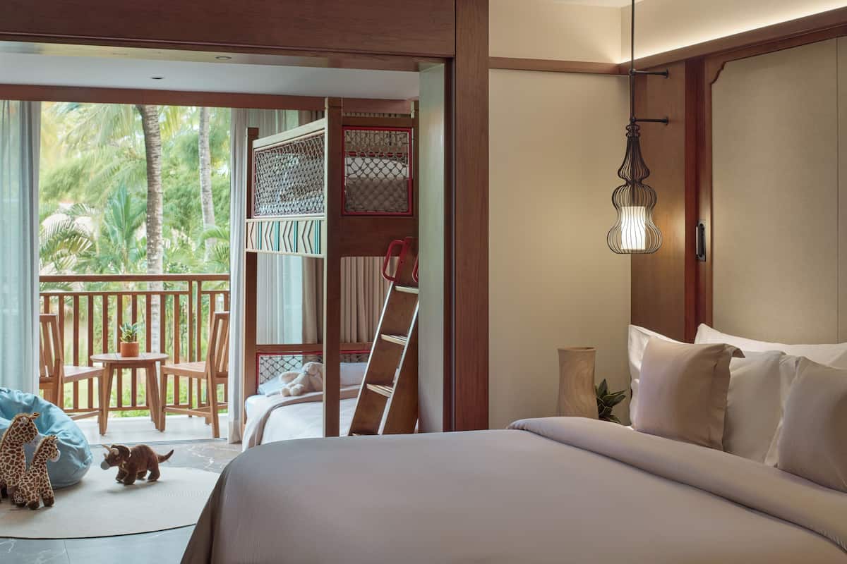 Ein Schlafzimmer mit Bett, einer Holzleiter, einem Balkon mit Stühlen und Blick auf Palmen.