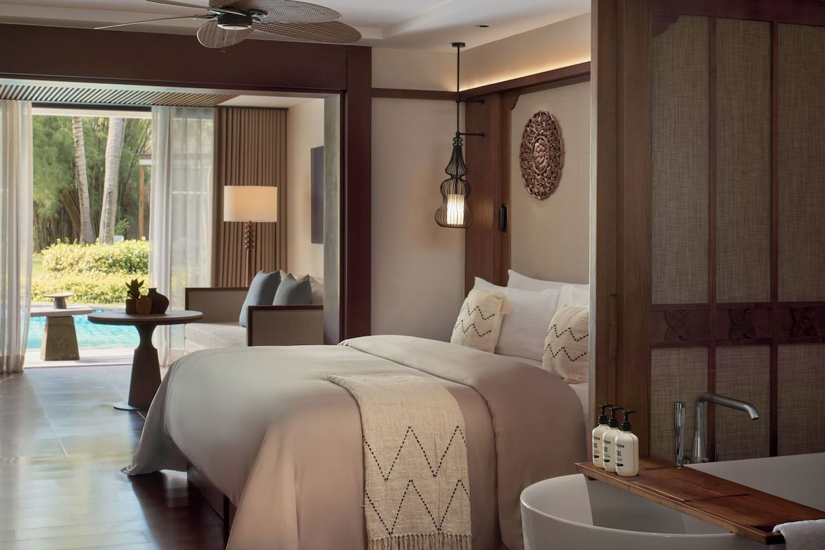 Ein Hotelzimmer mit Bett, Schreibtisch mit Toilettenartikeln, Badezimmer mit Badewanne und Blick ins Freie.