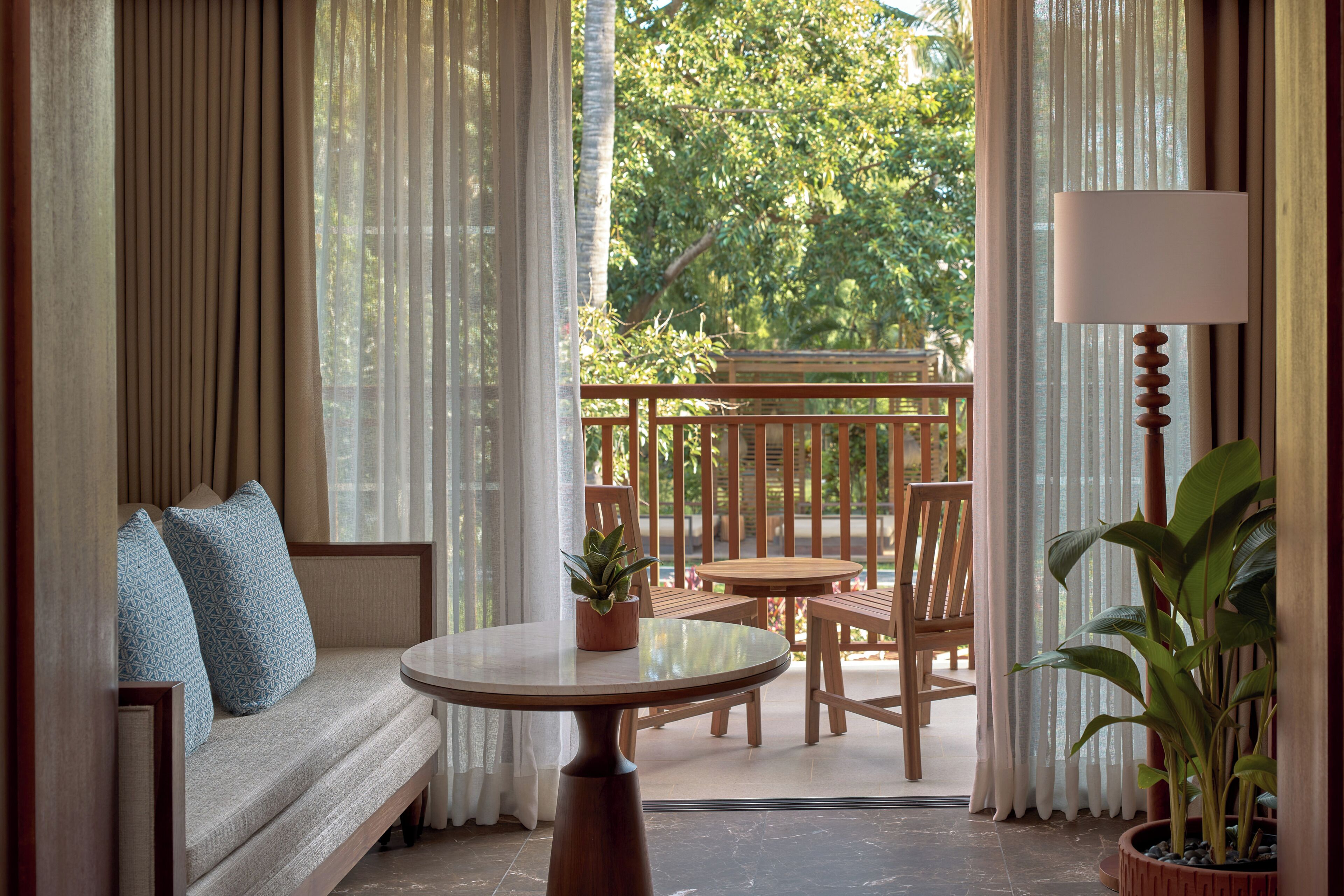 A balcony with a wooden table, chairs, a sofa with patterned cushions, and a potted plant.