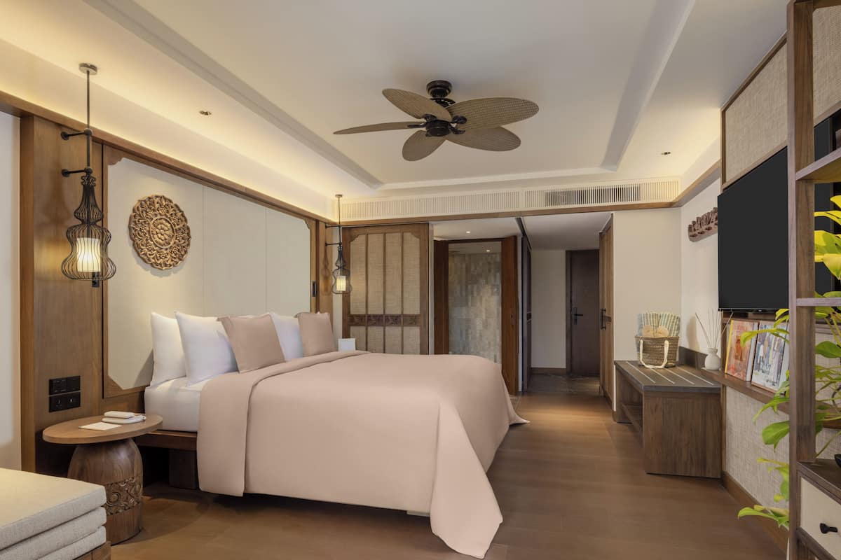 Ein modernes Hotelzimmer mit einem großen Bett, einem Deckenventilator, einem Fernseher und einem kleinen Nachttisch.