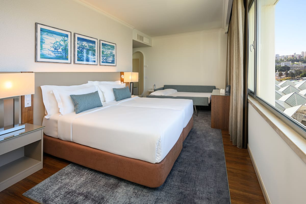 Habitación de hotel con una cama grande, una cama más pequeña, un escritorio y vistas de la ciudad.