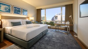 A modern hotel room with a large bed, a desk, and a view of the city.